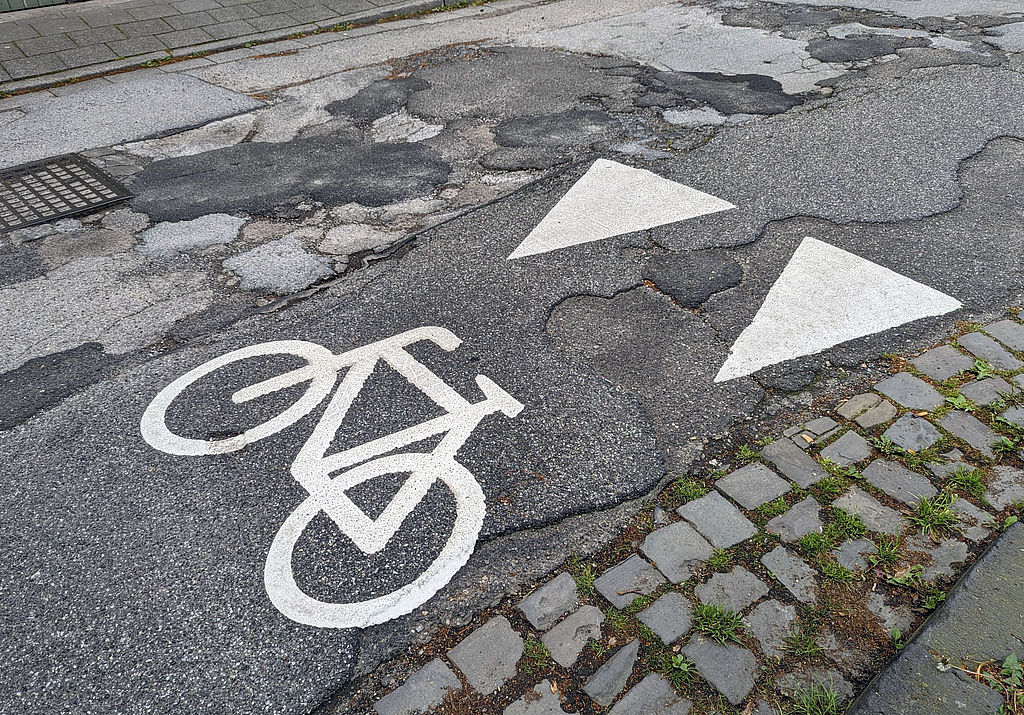 Rad-Markierung auf der Von-Werth-Straße in Mönchengladbach-Odenkirchen stark ausgebesserte Straße mit Huckeln, Löchern und Kopfsteinpflaster